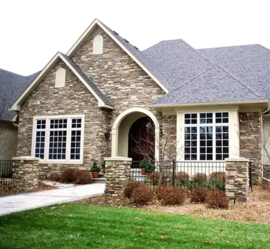A modern stone house with large windows, a front walkway, and a well-kept lawn.