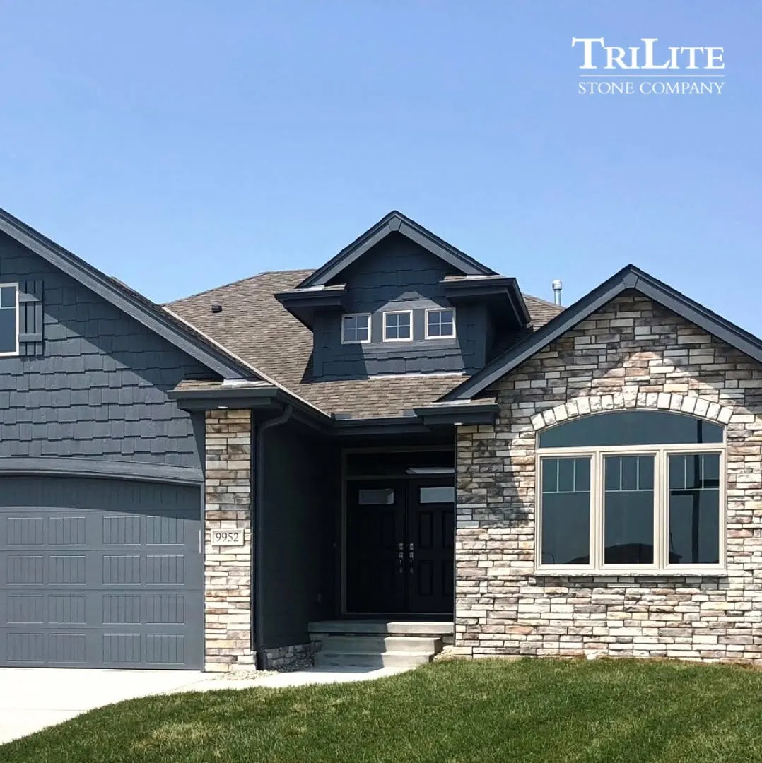 stone-3 Stone and shingle house exterior with dark trim, a two-car garage, and manicured lawn under clear sky.