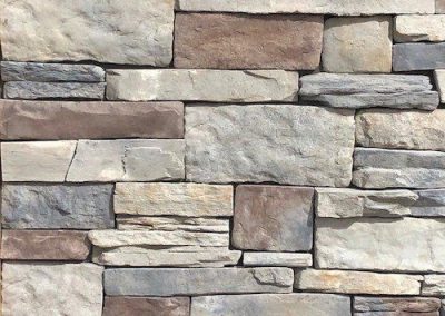 Varied rectangular stones in beige and gray shades form a neatly stacked stone wall.