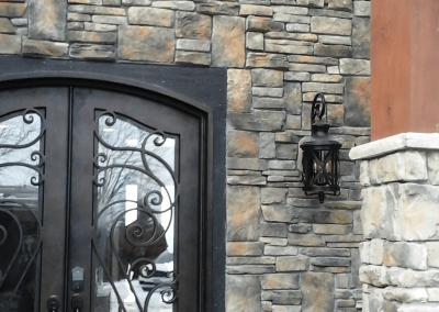 Stone house facade with black double doors, ornate ironwork, a lantern, and wooden beams.