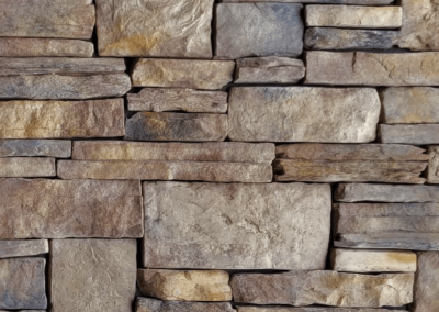 Brown, beige, and gray stacked stone wall with uneven rectangular stones in a brick-like pattern.