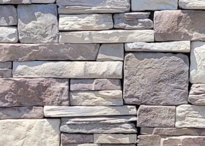 A close-up of a textured stone wall with rectangular and irregularly shaped light gray and beige stones.