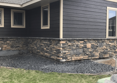 Dark house with stone siding and gravel area next to green grass. No plants or decorations visible.