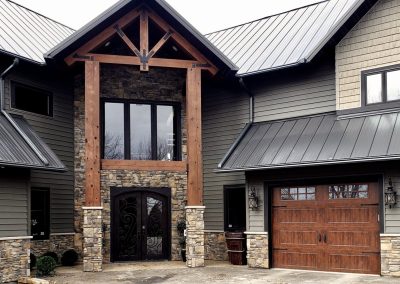 Modern house with stone and wood accents, large entryway, and a wooden garage door.