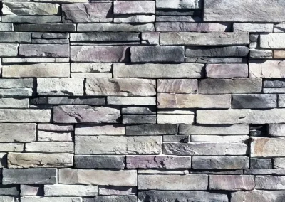 A close-up view of a gray and tan stacked stone wall with variously sized rectangular stones.