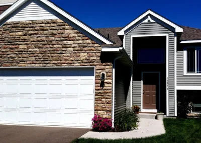 Modern suburban house with stone and siding, white garage door, brown front door, and small garden.