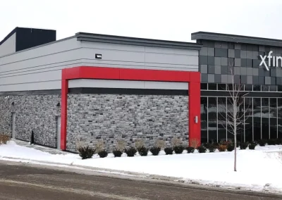 Modern Xfinity store with gray brick exterior, red trim, glass windows, and snow on the ground outside.