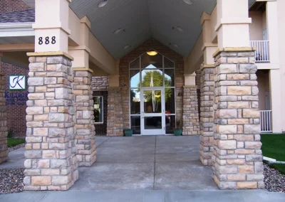 Stone pillars and double glass doors at the entrance of a building numbered 888, with a covered walkway.