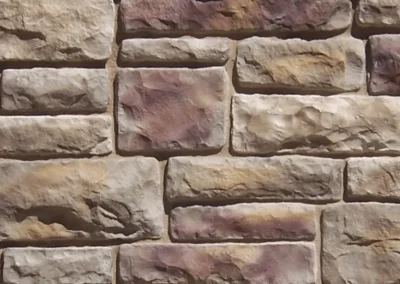 Tan and brown rectangular stones arranged in a stacked, brick-like pattern on a wall.