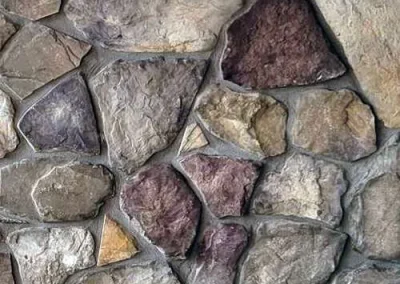 Close-up of a stone wall with irregularly shaped rocks in various earth tones and gray mortar.
