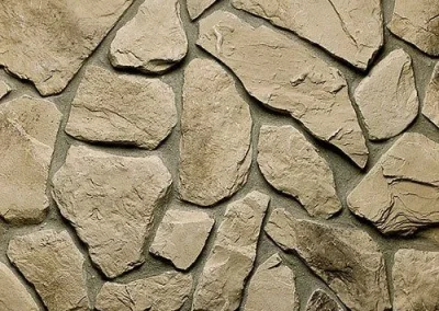 Irregular tan stones set in mortar, forming a rough, natural-looking stone wall pattern.