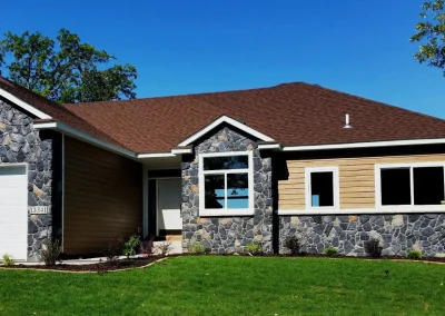 Single-story house with stone and wood exterior, brown roof, white garage door, and green lawn in front.