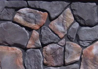 Irregularly-shaped gray and brown stones arranged closely together, forming a stone wall pattern.
