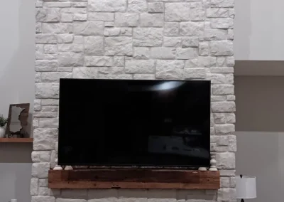 A white stone fireplace with a TV mounted above a wooden mantel and a black fireplace below.