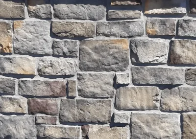 A close-up of a stone wall with various rectangular and irregularly shaped gray and beige stones.