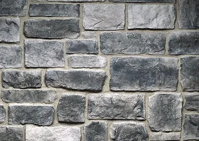 Gray rectangular stone bricks arranged in a staggered pattern, forming a textured wall surface.