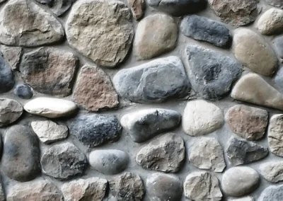 Close-up of a stone wall with variously shaped, smooth, and rough rocks set in gray mortar.