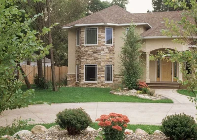 Two-story house with stone facade, curved driveway, and landscaped garden with shrubs and flowers.