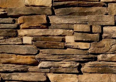 Stacked brown and tan rectangular stones form a rustic stone wall with visible texture and uneven surfaces.