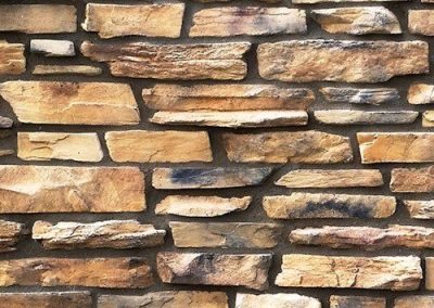Tan and brown stacked stone wall with uneven rectangular stones and visible texture.
