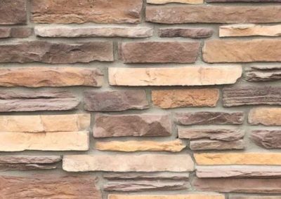 Tan and brown stone bricks arranged in a horizontal, staggered pattern on a wall.