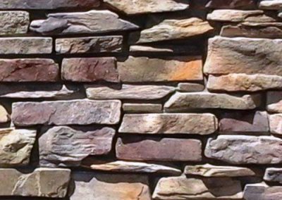 A close-up of a stone wall with rectangular, unevenly stacked stones in various earthy colors.