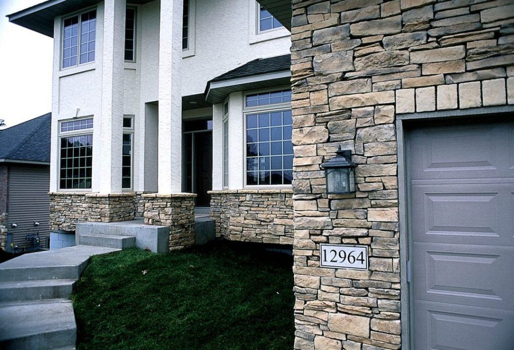 Modern house with stone siding, large windows, and the address number 12964 by a garage and light fixture.