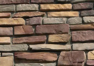 Close-up of a textured stone wall with rectangular, multicolored bricks arranged in a staggered pattern.