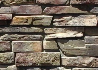 Close-up of an uneven stone wall with variously sized, rough-textured, rectangular stones.