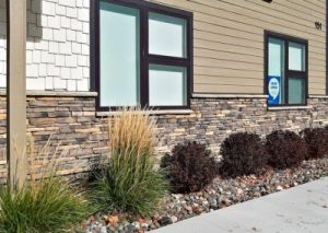 Prairie Ledgestone – Rustic Modern building exterior with stone and siding, frosted windows, and landscaping with grass and shrubs.