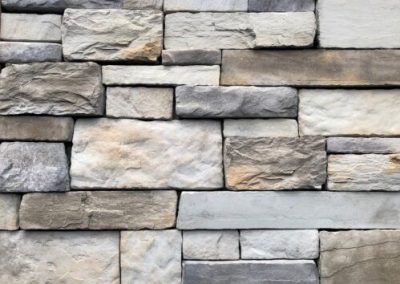 A close-up of a stone wall with rectangular gray, beige, and tan stones arranged in a brick pattern.