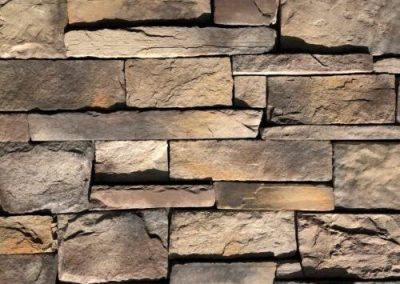 Stacked rectangular stones of varying sizes and earth tones, forming a textured wall pattern.