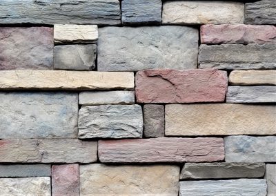 A close-up of a wall made of rectangular, multicolored stacked stone bricks.