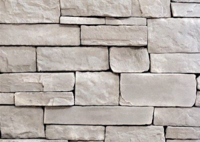 Close-up of a beige stone brick wall with rectangular stones stacked in a horizontal pattern.