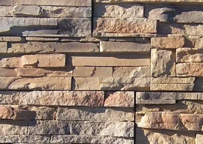 Tan and gray rectangular stones stacked in a horizontal, interlocking pattern on a wall.