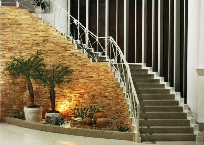 Indoor staircase with a stone wall, potted plants, and decorative pots arranged under the stairs.