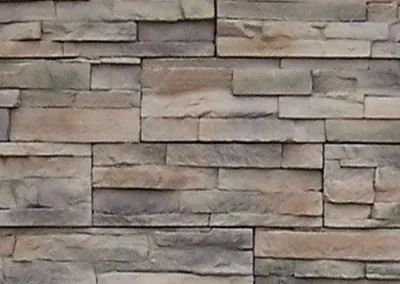 Tan and gray rectangular stone bricks arranged in a staggered horizontal pattern on a wall.