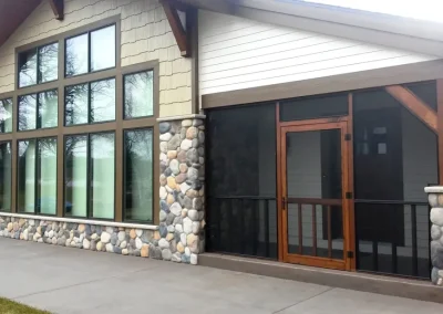 Modern house exterior with large windows, stone accents, and a screened porch with wooden frame.