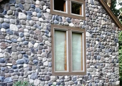 Stone cottage wall with two square windows above a large rectangular window, surrounded by greenery.
