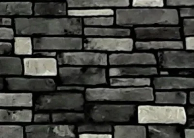 A wall made of rectangular, unevenly stacked black and gray bricks.