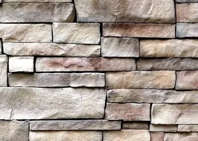 Close-up of a stone brick wall with rectangular, unevenly sized tan and brown stones stacked together.