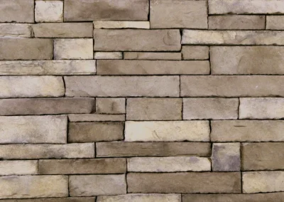 Tan stone bricks arranged in a horizontal pattern, forming a textured and uneven wall surface.
