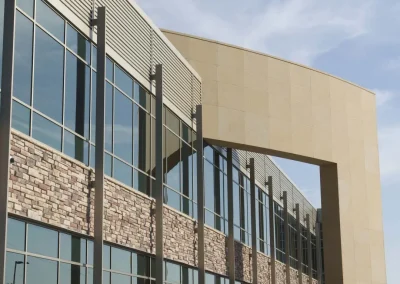 Modern building with large windows, stone accents, and a tall beige arch against a blue sky.