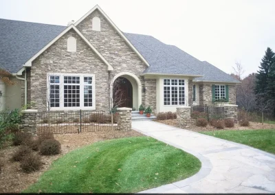 Stone house with large windows, green lawn, and a curved walkway leading to the front entrance.
