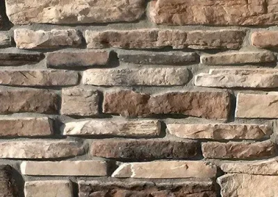 A close-up of a stone wall featuring various rectangular brown and beige stones stacked in an irregular pattern.