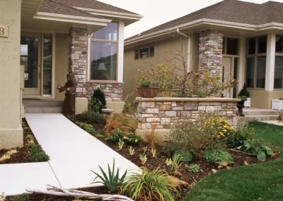 Modern house with stone accents, landscaped garden, concrete walkway, and green lawn in front yard.
