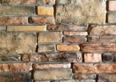 A close-up of a textured stone wall with various shapes and shades of brown, tan, and gray stones.