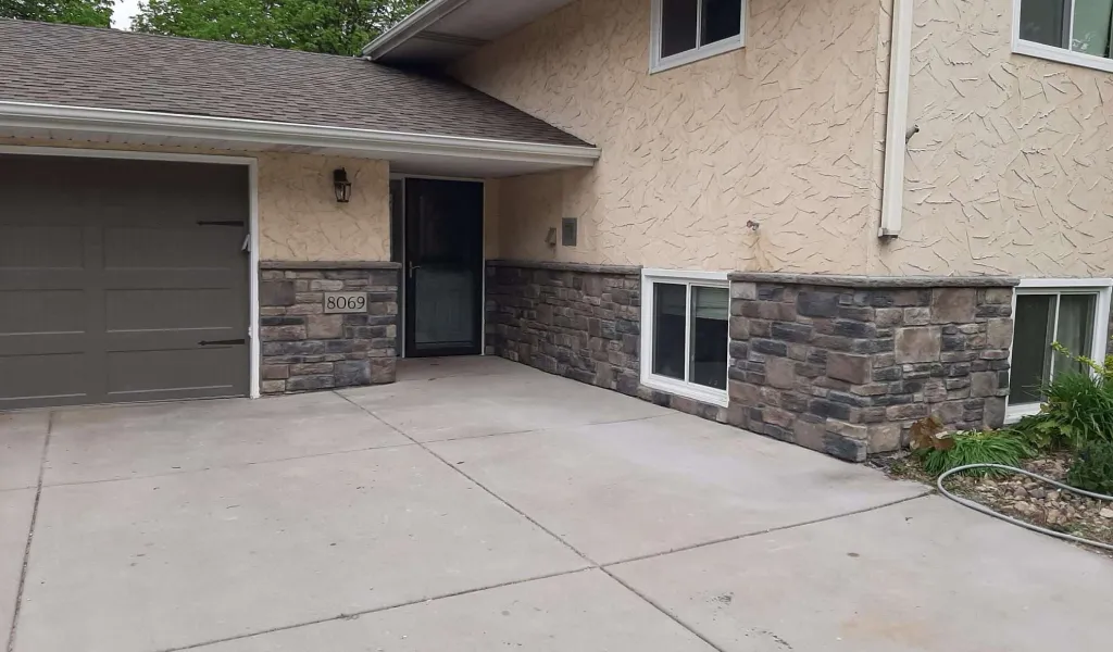 Front view of a beige house with stone accents, a garage door, and a concrete driveway.