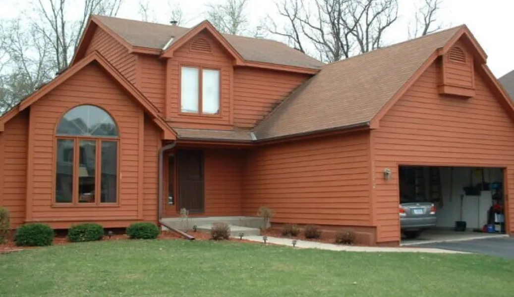 Two-story orange house with large windows, attached garage, and a car parked inside; green lawn in front.