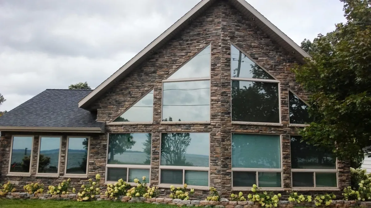 A modern house with large triangular windows and a stone exterior, surrounded by greenery.